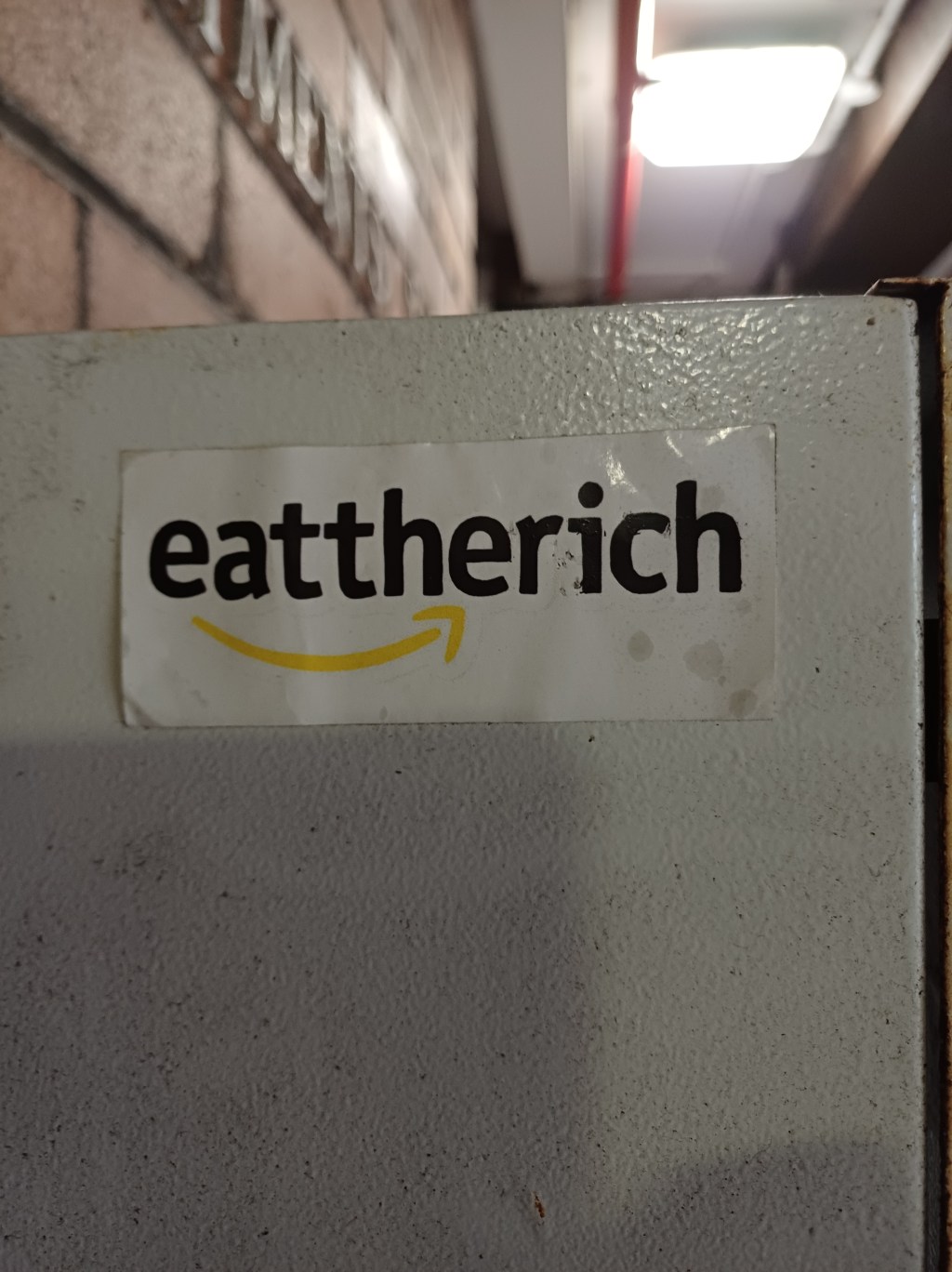 sticker in apartment block reading "eat the rich" in a font and design parody of the amazon "smile" logo