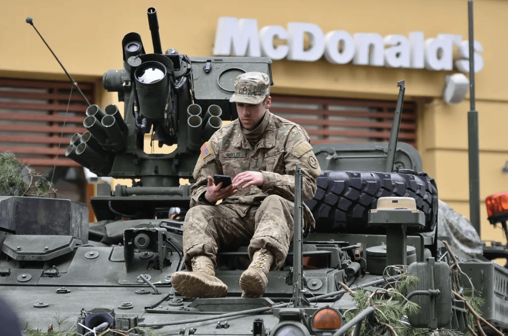 Soldier sitting on army tank outside McDonald's fastfood restaurant looking at his cellphone